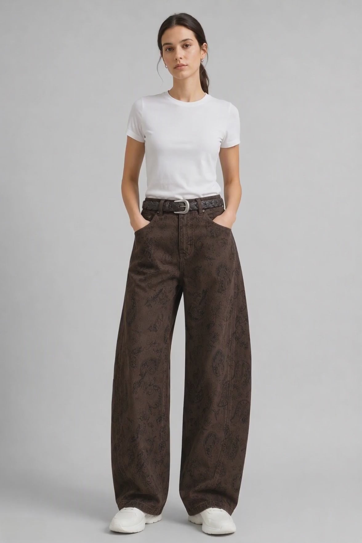 Model wearing Paisley-Jacquard Curved-Leg Jeans in Brown, walking and turning to show the curved-leg fit and all-over paisley jacquard pattern.