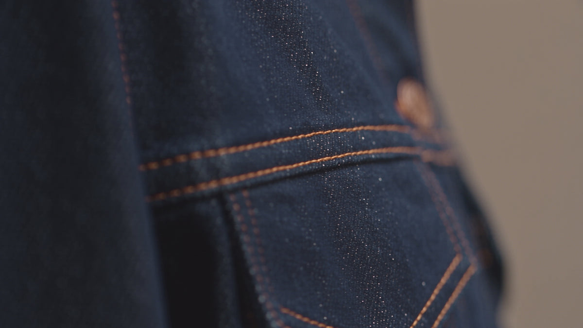 QAYQEY brand transition video, 16:9 cinematic footage showing premium indigo denim fabric details, a European female model walking through a minimalist concrete art gallery, and deep blue abstract ink-wash brushstroke shadows on the wall. Pure visual storytelling, Oriental aesthetics combined with modern denim fashion.